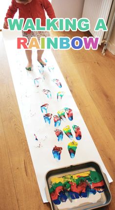 a young child standing on top of a wooden floor next to a white sheet with colorful handprints