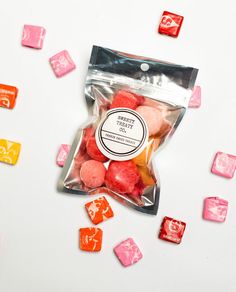 candy candies are in a bag and scattered around on a white surface with pink and yellow squares