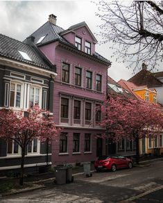 a red car parked on the side of a road next to tall buildings with pink flowers