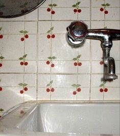 a white sink sitting under a faucet next to a wall with cherries on it