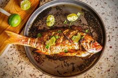 grilled fish in a pan with limes on the side