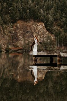 a bride and groom standing on a dock in the middle of a lake surrounded by trees