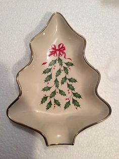 a christmas tree shaped dish with red bows and holly leaves on it's side