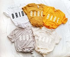 three t - shirts that say bride and babe are on a white bed with yellow sheets