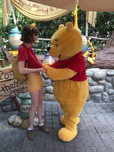 a woman standing next to a giant winnie the pooh mascot