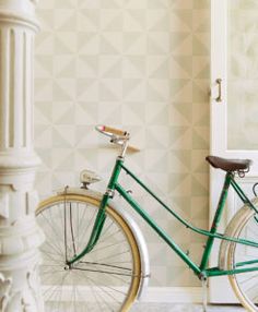 a green bicycle parked in front of a white wall with geometric designs on it's side