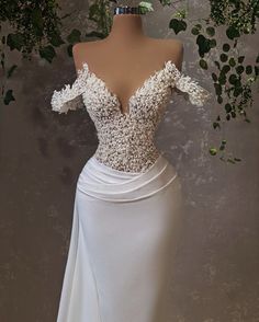 a white wedding dress with flowers on the shoulders and off the shoulder, is displayed in front of a mannequin