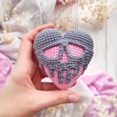 a hand holding a crocheted heart with a skull on it