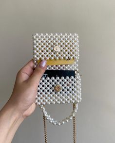 a hand holding a white beaded purse with pearls on the bottom and gold chain