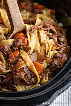 a crock pot filled with pasta and beef, carrots and meat sauce is being stirred by a wooden spoon