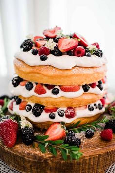 a cake with berries and whipped cream is on top of a wooden platter, surrounded by greenery