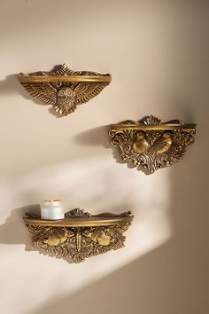 two gold wall mounted shelves with candles on them