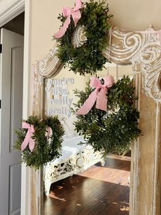 wreaths are hung on the wall in front of an ornate mirror with pink bows