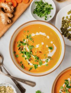 several bowls of carrot soup with garnishes and spoons on the side