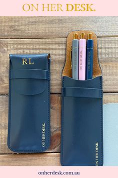 a blue leather case with pens and pencils in it on a wooden table next to a pen holder