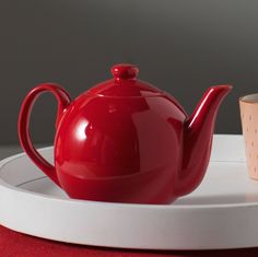 a red teapot sitting on top of a white plate next to a small cup