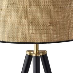 a black and gold tripod lamp with a beige shade on the top, against a white background