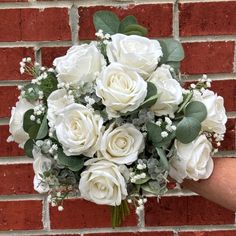 a bridal bouquet with white roses and baby's breath is held against a brick wall