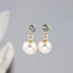 "These modern pearl drop earrings feature near round white freshwater pearls hanging from 14k yellow gold dangles with tiny aquamarines bezel set above. These small drop earrings have post backs. They are made to order. Each round pearl is unique and measures approximately 6.5mm in diameter. The pearls hang from solid 14k yellow gold dangles. A gorgeous 3mm aquamarine is bezel set above, with a white gold post behind. These earrings come with solid gold butterfly backs. Aquamarine is the birthst Blue Round Jewelry With Pearl Charm, Classic Blue Round Pearl Earrings, Elegant Round Aquamarine Earrings, Blue Pearl Wedding Earrings, Fine Jewelry, Blue Pearl Charm Drop Earrings, Small Drop Earrings, Earrings Round, March Birthstone, White Freshwater Pearl