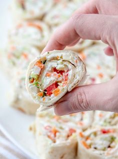 a hand holding a vegetable wrap over a white plate