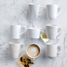 coffee cups and saucers are arranged on a marble counter top, with one empty cup in the middle