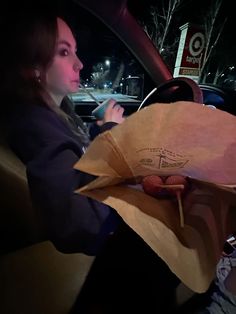 a woman sitting in a car holding a paper bag