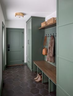 a hallway with green cabinets and wooden bench next to it's coat rack on the wall