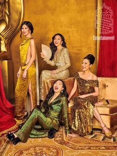 three women in gold and green dresses sitting on a couch with one woman holding a fan