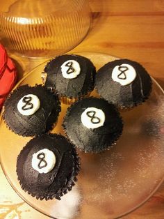 four cupcakes with black frosting and white numbers on them sitting on a plate