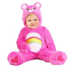 a baby in a pink teddy bear costume sitting on the ground with a rainbow t - shirt