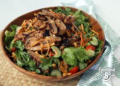 a wooden bowl filled with meat and veggies on top of a bamboo mat