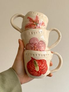 a hand holding three coffee mugs with designs on them