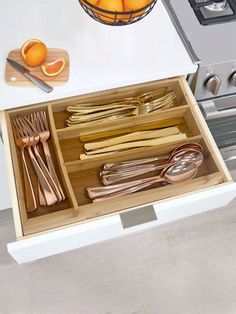 an open drawer with utensils and oranges in it