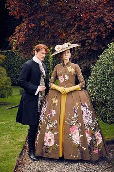 a man and woman dressed in period clothing standing next to each other on the grass