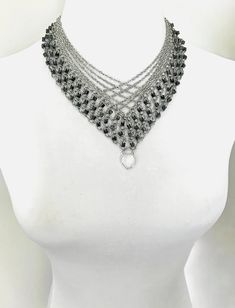 This v shaped beaded chainmail necklace is made of stainless steel cable chains, stainless steel jump rings and glass beads. The glass beads are cube-shaped and have a glossy black marble style finish, including various shades of black, gray and pewter. Overlapping smaller, textured chains give this piece the ultimate layered look, sure to turn an otherwise basic outfit into a chic ensemble. At the bottom of the v shape is a crystal quartz pendant bezeled in sterling silver. The necklace is abou Black Metal Chainmail Necklace, V Shaped Necklace, Chainmaille Jewelry Patterns, Chain Maille Patterns, Chainmail Necklace, Chain Maille Jewelry, Quartz Crystal Pendant, Chain Maille, Layered Chains