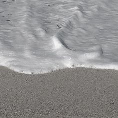 a bird is standing on the sand near the water's edge, with waves coming in