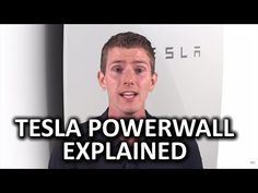 a man in black shirt standing next to a white wall with tesla logo on it