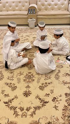 four young men sitting on the floor in front of a couch and rug, all dressed in white