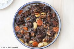 a blue bowl filled with meat and vegetables on top of a wooden table next to a white plate