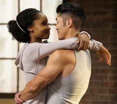 a man and woman dance together in front of a brick wall, with their arms around each other