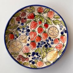 a bowl with fruit painted on it sitting on top of a white tablecloth covered wall