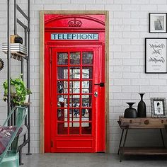 a red phone booth sitting in front of a white brick wall next to a wooden table