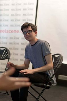 a young man sitting in a chair with his hand out to another person who is pointing at him