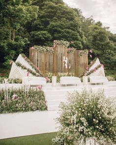 an outdoor wedding setup with white chairs and pink flowers on the back wall, surrounded by greenery