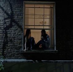 two people sitting on a window sill at night