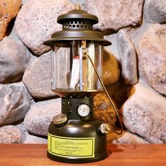 an old fashioned lantern sitting on top of a wooden table next to some large rocks