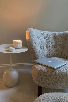 a laptop computer sitting on top of a white chair next to a table with a candle