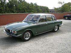 an old green car parked in a parking lot