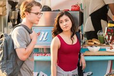 a man and woman standing in front of a hot dog stand with food on it