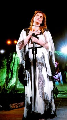 a woman standing on top of a stage wearing a white and black dress holding a microphone